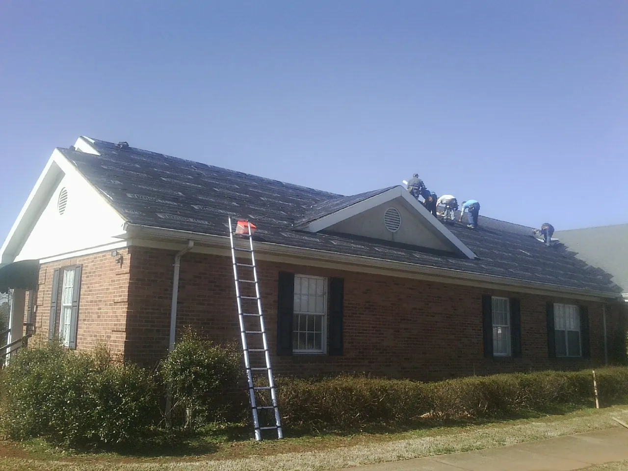 Crew tearing shingles off a brick ranch roof with a ladder set — Metal Roof Repair work by our crew in Williamsburg