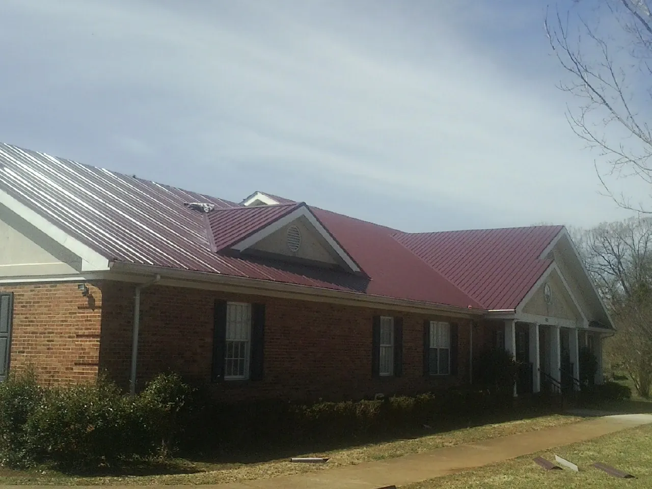Red metal roof with gabled entries on a long brick building, from a Hail Damage Roof Repair job in Williamsburg
