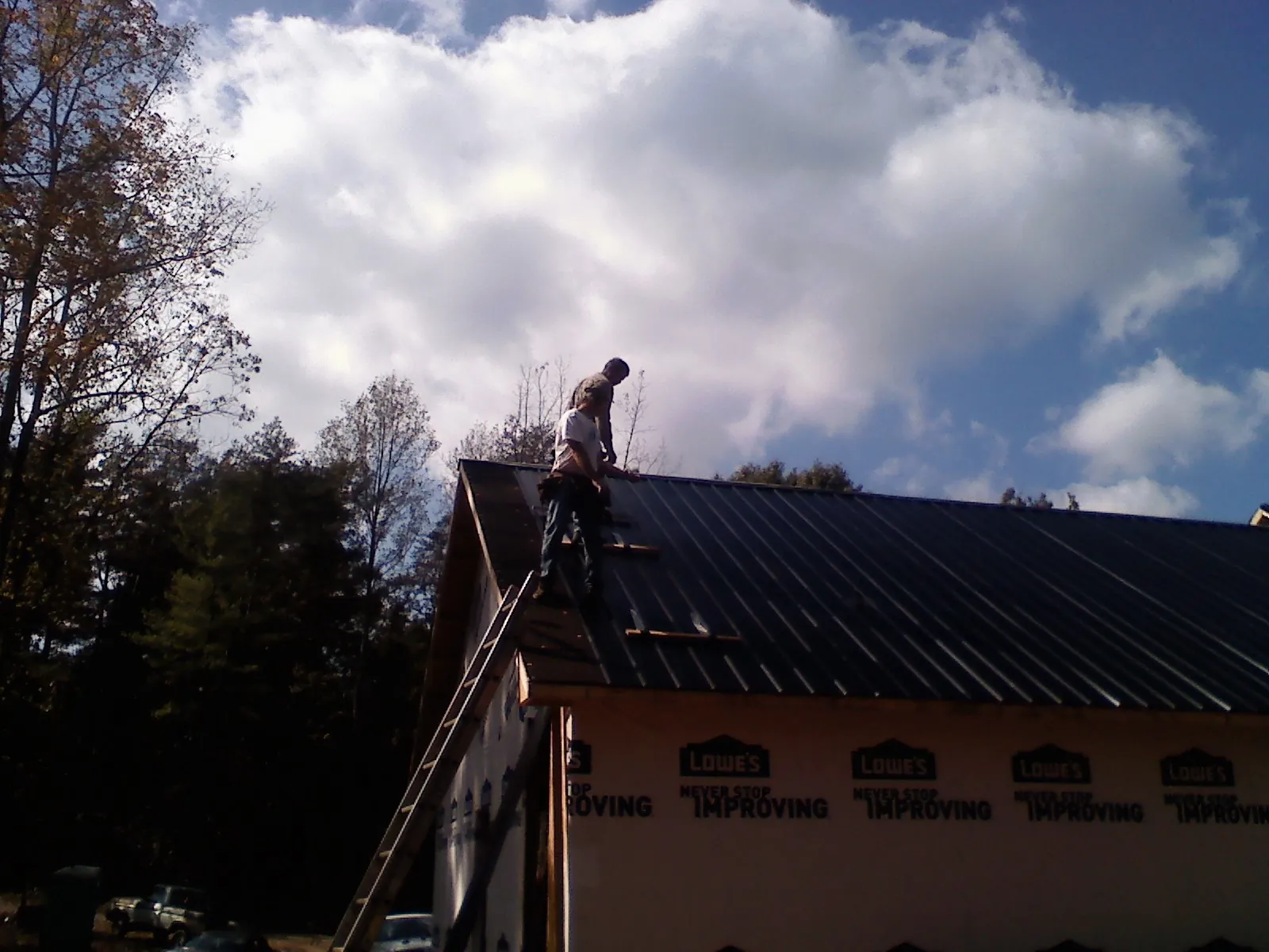 Roofer fastening dark metal panels high against a cloudy sky, from a Roof Inspection job in Williamsburg